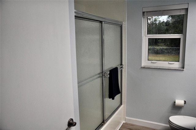 bathroom featuring toilet, wood-type flooring, and bath / shower combo with glass door