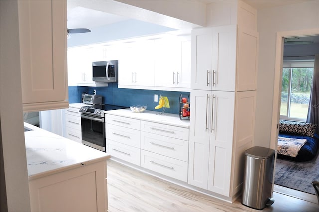 kitchen with light stone countertops, stainless steel appliances, tasteful backsplash, light hardwood / wood-style floors, and white cabinets