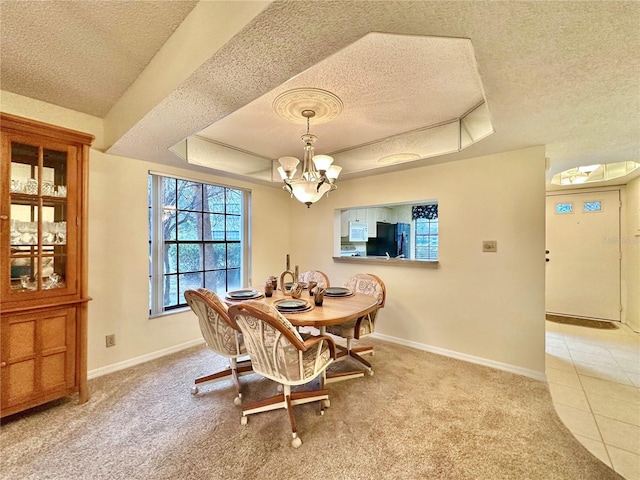 dining area with light carpet, a textured ceiling, a tray ceiling, and a chandelier