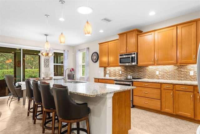 kitchen with pendant lighting, a center island with sink, sink, light stone countertops, and stainless steel appliances