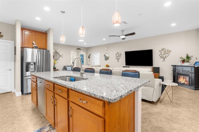 kitchen featuring ceiling fan, sink, light stone counters, pendant lighting, and a kitchen island with sink