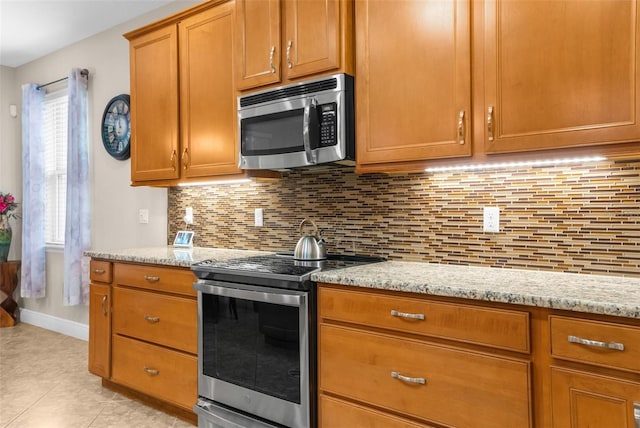 kitchen featuring light stone countertops, decorative backsplash, light tile patterned floors, and stainless steel appliances