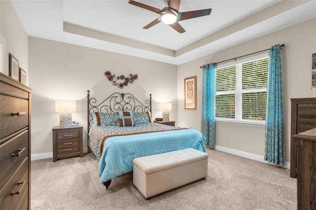 bedroom featuring light colored carpet, a raised ceiling, and ceiling fan