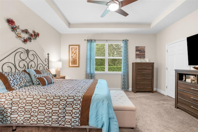 bedroom with ceiling fan, light colored carpet, and a tray ceiling