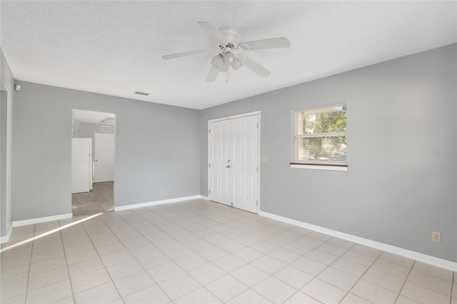 empty room featuring a textured ceiling, ceiling fan, and light tile patterned flooring