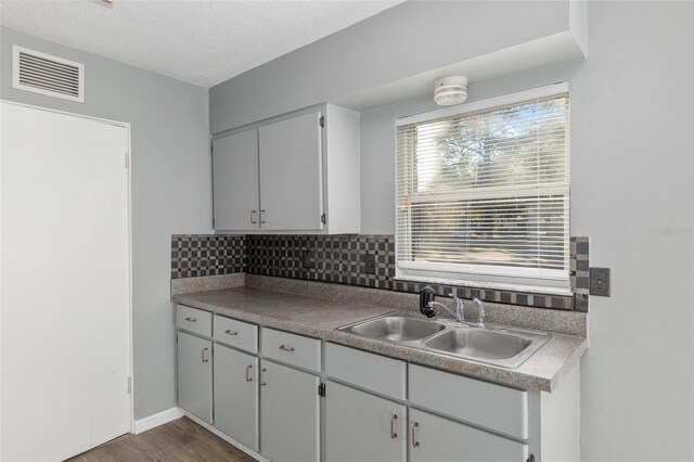 kitchen featuring dark hardwood / wood-style flooring, backsplash, a textured ceiling, sink, and gray cabinets