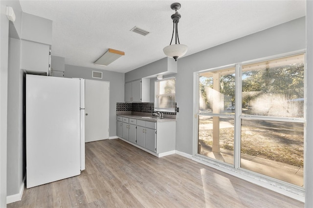 kitchen with decorative backsplash, sink, light hardwood / wood-style flooring, white fridge, and hanging light fixtures