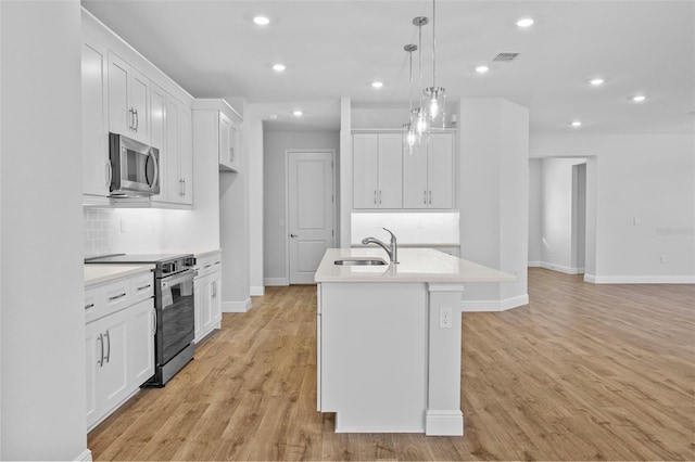 kitchen featuring white cabinets, appliances with stainless steel finishes, decorative light fixtures, and an island with sink