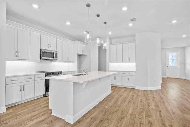 kitchen featuring appliances with stainless steel finishes, a kitchen island with sink, decorative light fixtures, white cabinets, and light hardwood / wood-style floors