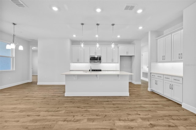 kitchen with white cabinetry, a center island with sink, hanging light fixtures, and light hardwood / wood-style floors