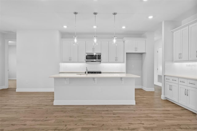 kitchen featuring light hardwood / wood-style flooring, backsplash, pendant lighting, a kitchen island with sink, and white cabinets