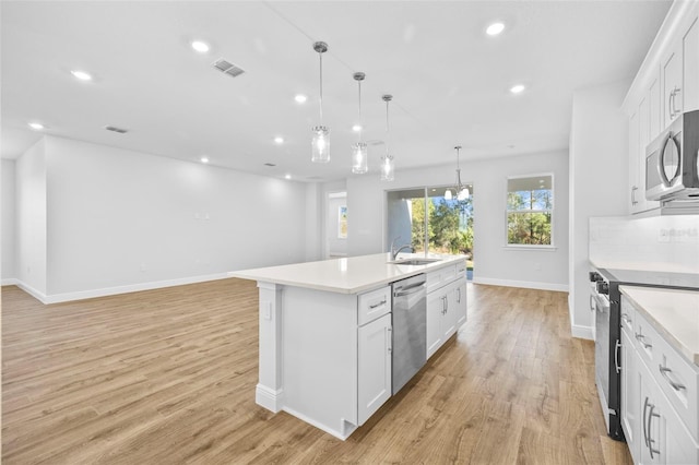 kitchen featuring a kitchen island with sink, sink, decorative light fixtures, white cabinetry, and stainless steel appliances