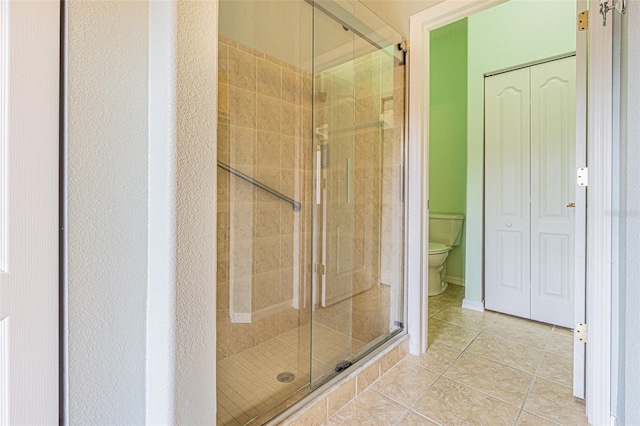 bathroom featuring toilet, tile patterned flooring, and a shower with shower door