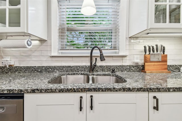 kitchen featuring decorative backsplash, white cabinets, glass insert cabinets, dark stone countertops, and a sink