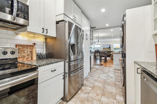 kitchen with stainless steel appliances, tasteful backsplash, dark stone countertops, and white cabinetry