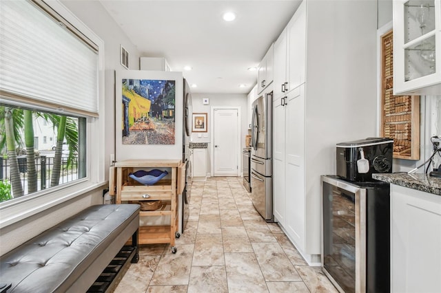 kitchen featuring beverage cooler, white cabinetry, freestanding refrigerator, dark stone countertops, and glass insert cabinets