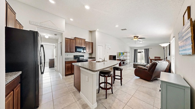 kitchen featuring a kitchen bar, ceiling fan, black appliances, light tile patterned floors, and a center island with sink