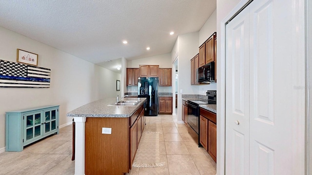 kitchen featuring light tile patterned floors, sink, an island with sink, and black appliances