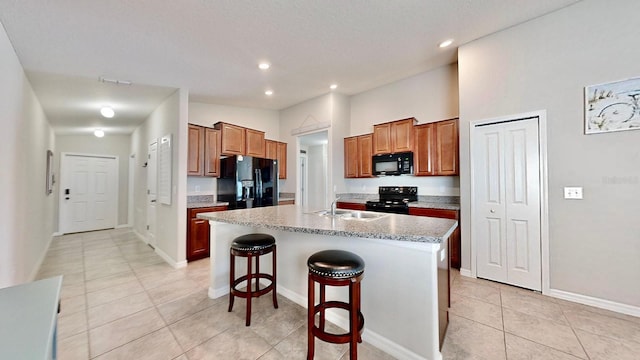 kitchen featuring a kitchen breakfast bar, a kitchen island with sink, light tile patterned floors, and black appliances