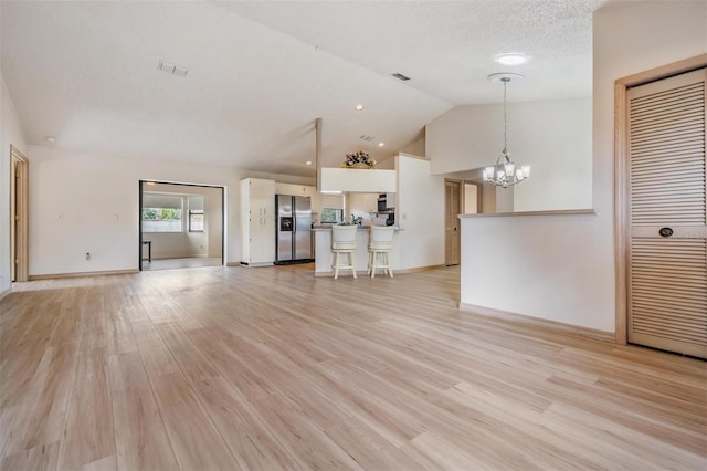 unfurnished living room with light hardwood / wood-style flooring, a notable chandelier, and lofted ceiling