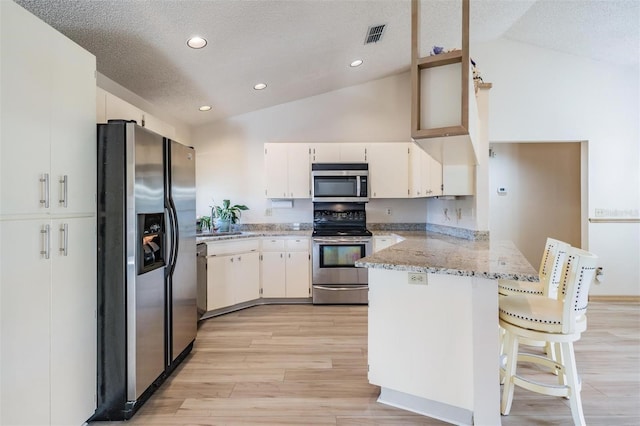 kitchen featuring a kitchen bar, light stone countertops, white cabinetry, kitchen peninsula, and stainless steel appliances