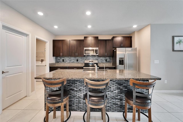 kitchen featuring a kitchen bar, appliances with stainless steel finishes, dark brown cabinetry, and an island with sink