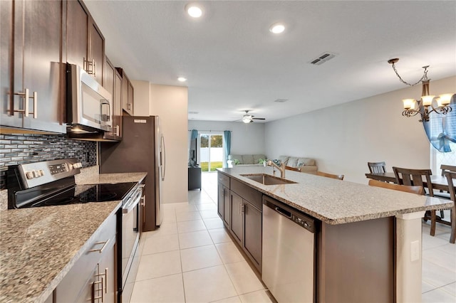 kitchen featuring backsplash, ceiling fan with notable chandelier, stainless steel appliances, a kitchen island with sink, and sink