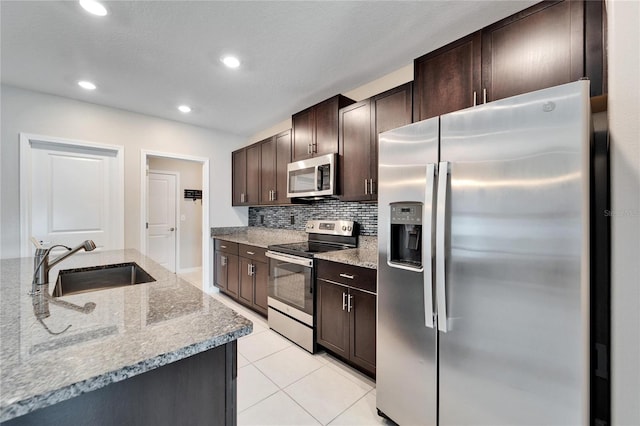 kitchen with light stone countertops, appliances with stainless steel finishes, backsplash, dark brown cabinets, and sink