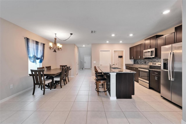 kitchen with appliances with stainless steel finishes, light stone counters, a kitchen island with sink, sink, and a chandelier