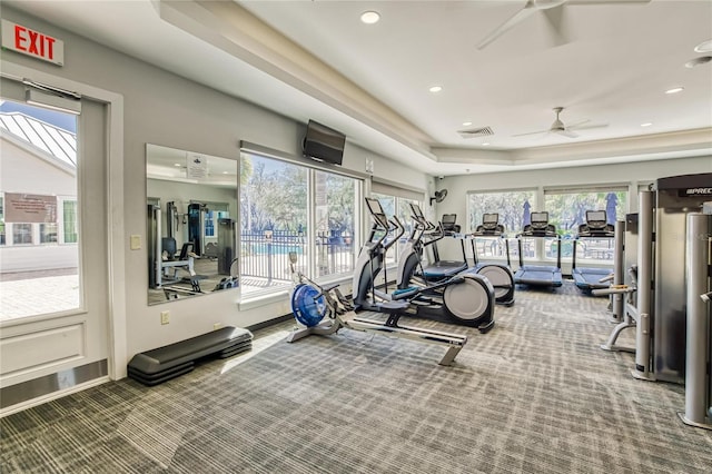 workout area featuring carpet flooring, ceiling fan, and a tray ceiling