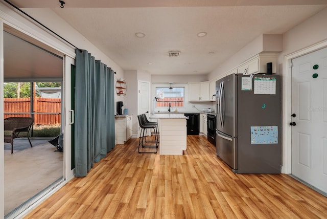 kitchen with a breakfast bar, black appliances, white cabinets, light hardwood / wood-style floors, and a kitchen island