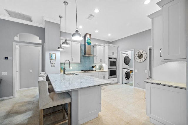 kitchen with sink, hanging light fixtures, appliances with stainless steel finishes, stacked washer / drying machine, and white cabinetry