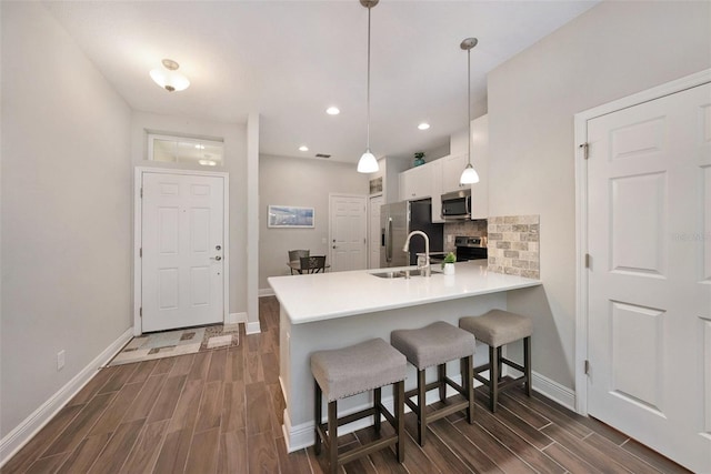 kitchen featuring pendant lighting, kitchen peninsula, a kitchen bar, white cabinetry, and stainless steel appliances