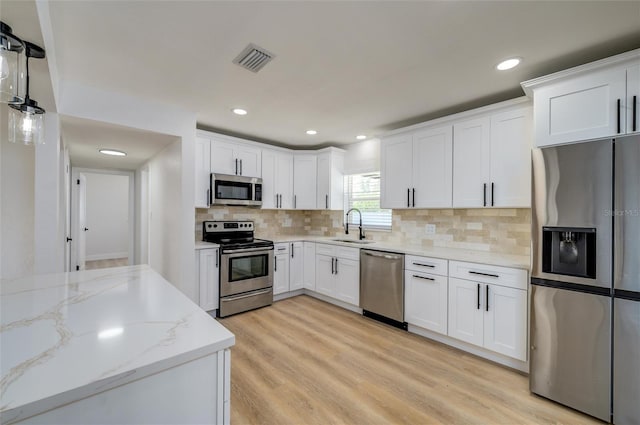 kitchen with white cabinets, decorative light fixtures, light stone countertops, and appliances with stainless steel finishes