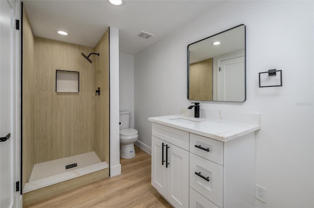 bathroom featuring a tile shower, vanity, hardwood / wood-style flooring, and toilet