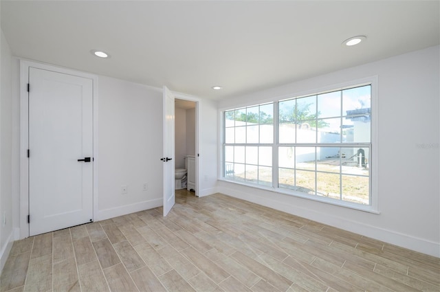 unfurnished bedroom featuring ensuite bathroom, light hardwood / wood-style flooring, and multiple windows