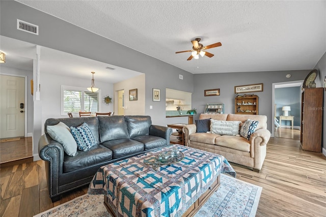 living room with a textured ceiling, light hardwood / wood-style flooring, ceiling fan, and lofted ceiling