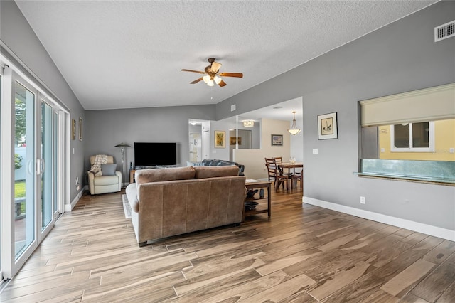 living room with ceiling fan, a textured ceiling, and vaulted ceiling