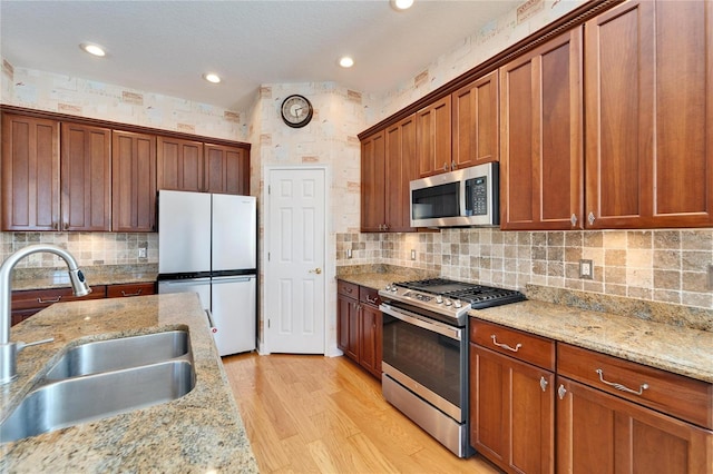 kitchen featuring light stone counters, light hardwood / wood-style flooring, decorative backsplash, appliances with stainless steel finishes, and sink