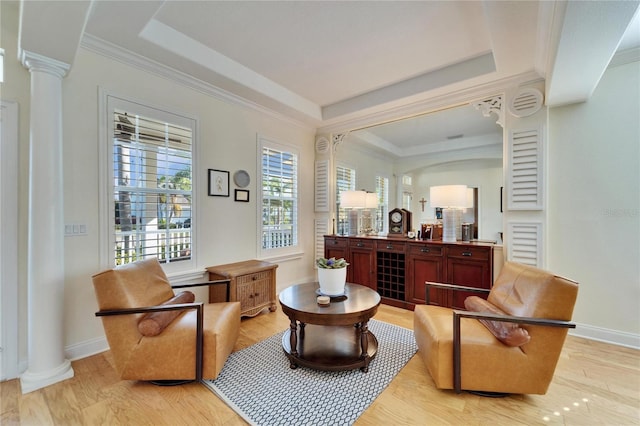 sitting room with decorative columns, a raised ceiling, light wood-type flooring, and ornamental molding