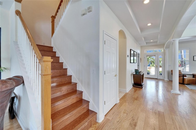 foyer entrance featuring a raised ceiling, french doors, light wood-type flooring, and decorative columns