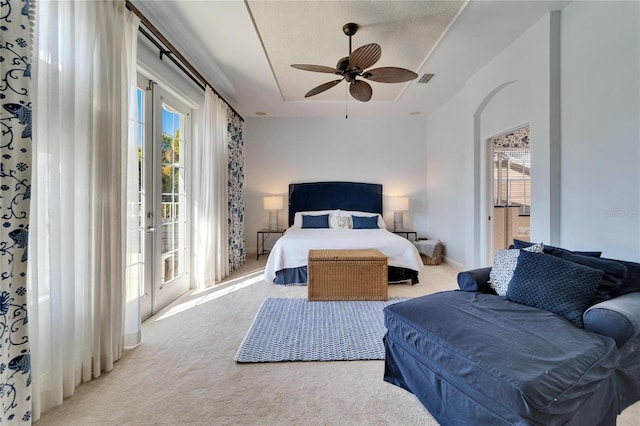 carpeted bedroom featuring access to exterior, ceiling fan, and a tray ceiling