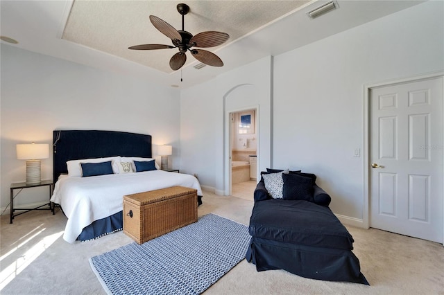 carpeted bedroom with ensuite bathroom, a raised ceiling, and ceiling fan