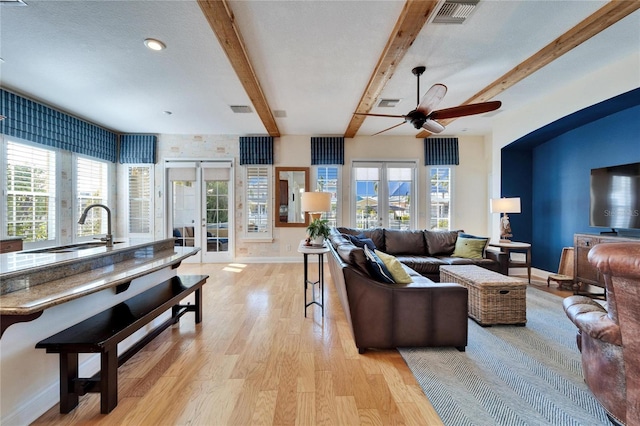 living room featuring sink, light hardwood / wood-style flooring, french doors, and beamed ceiling