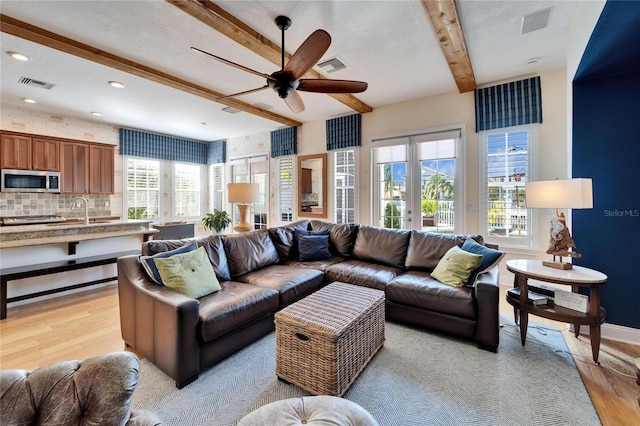 living room featuring light wood-type flooring, beam ceiling, and ceiling fan