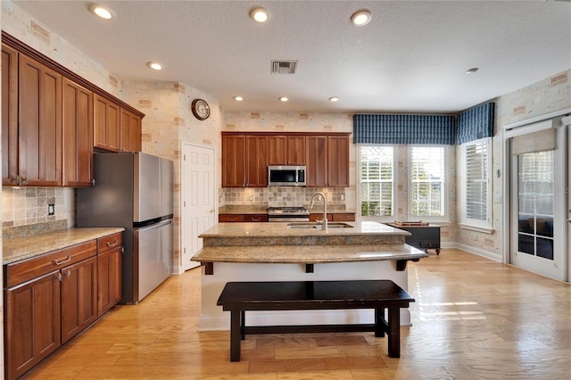 kitchen featuring appliances with stainless steel finishes, an island with sink, light stone countertops, a kitchen bar, and sink