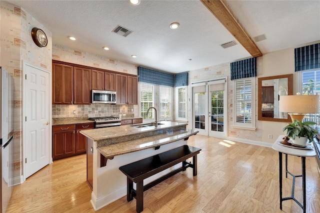 kitchen with a center island with sink, stainless steel appliances, a kitchen bar, beam ceiling, and sink