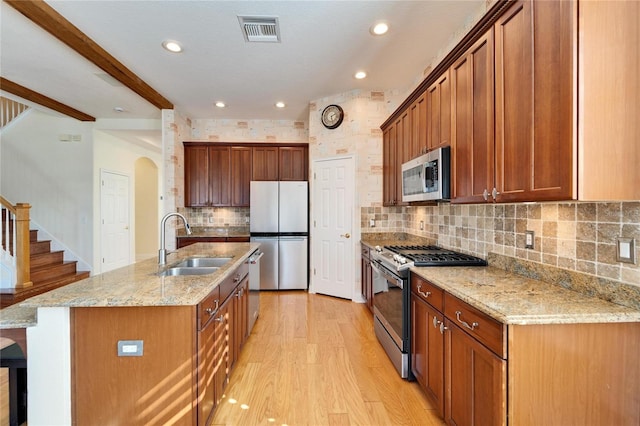 kitchen featuring stainless steel appliances, sink, light hardwood / wood-style flooring, a center island with sink, and beam ceiling