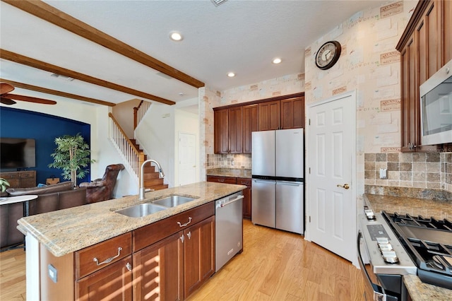 kitchen featuring a center island with sink, backsplash, appliances with stainless steel finishes, beamed ceiling, and sink