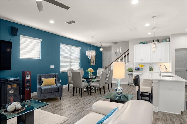 living room with ceiling fan with notable chandelier, sink, and light wood-type flooring